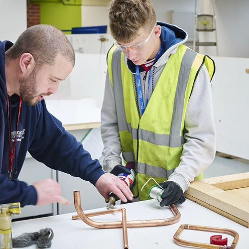 A teacher instructing a student to assemble plumbing pipes