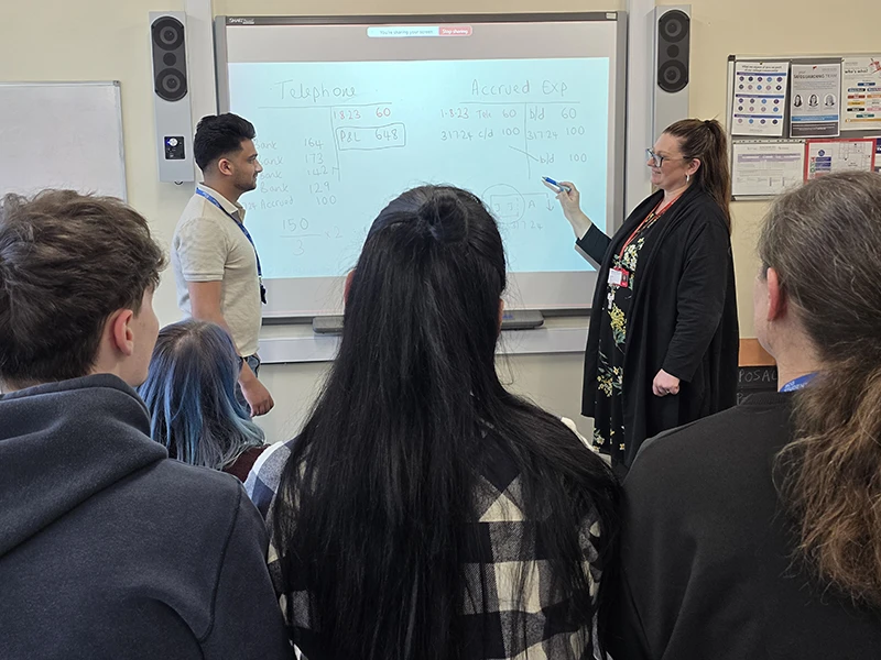 Teacher at whiteboard explaining accounting equations to class