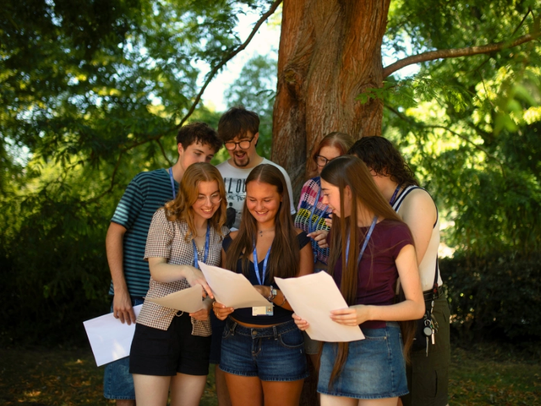 A group of students under a tree reading from sheets of paper